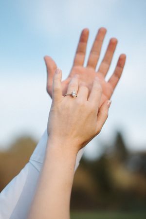 A hand with an engagement ring is raised against a bright blue sky background.