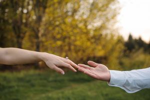 Close up of hands reaching towards each other against blurred autumn foliage background.