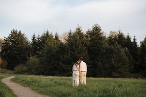 A couple walks hand in hand along a serene nature trail surrounded by evergreen trees at dusk.