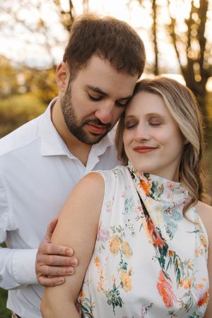A couple embraces in a tender moment outdoors during golden hour while wearing white and floral attire.