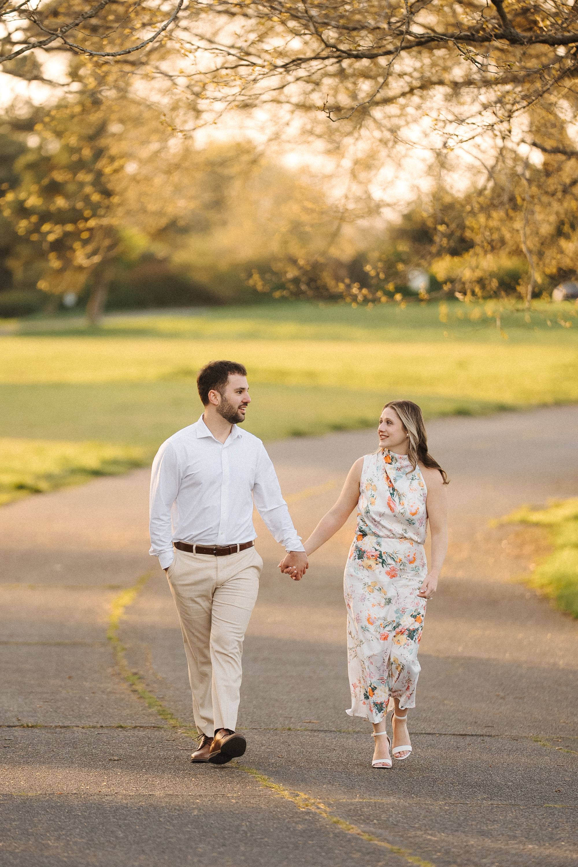 A couple holds hands while walking together on a path during golden hour sunset.