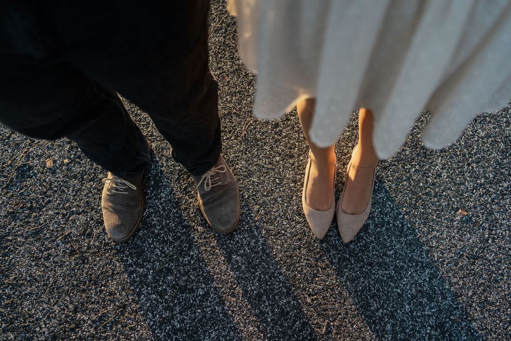 Close-up view of feet in formal shoes standing on textured pavement at sunset.