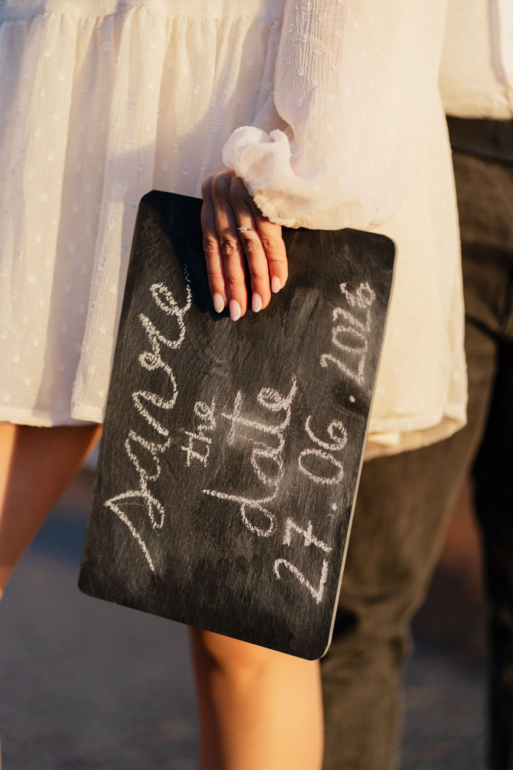 Close-up view of a small chalkboard slate with handwritten text being held in someone's hand.