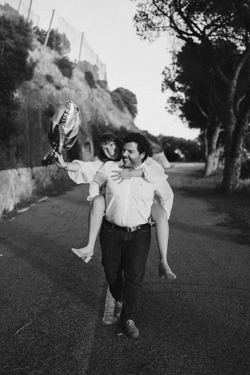 Black and white photo series of a couple playfully walking and embracing on a tree-lined path.
