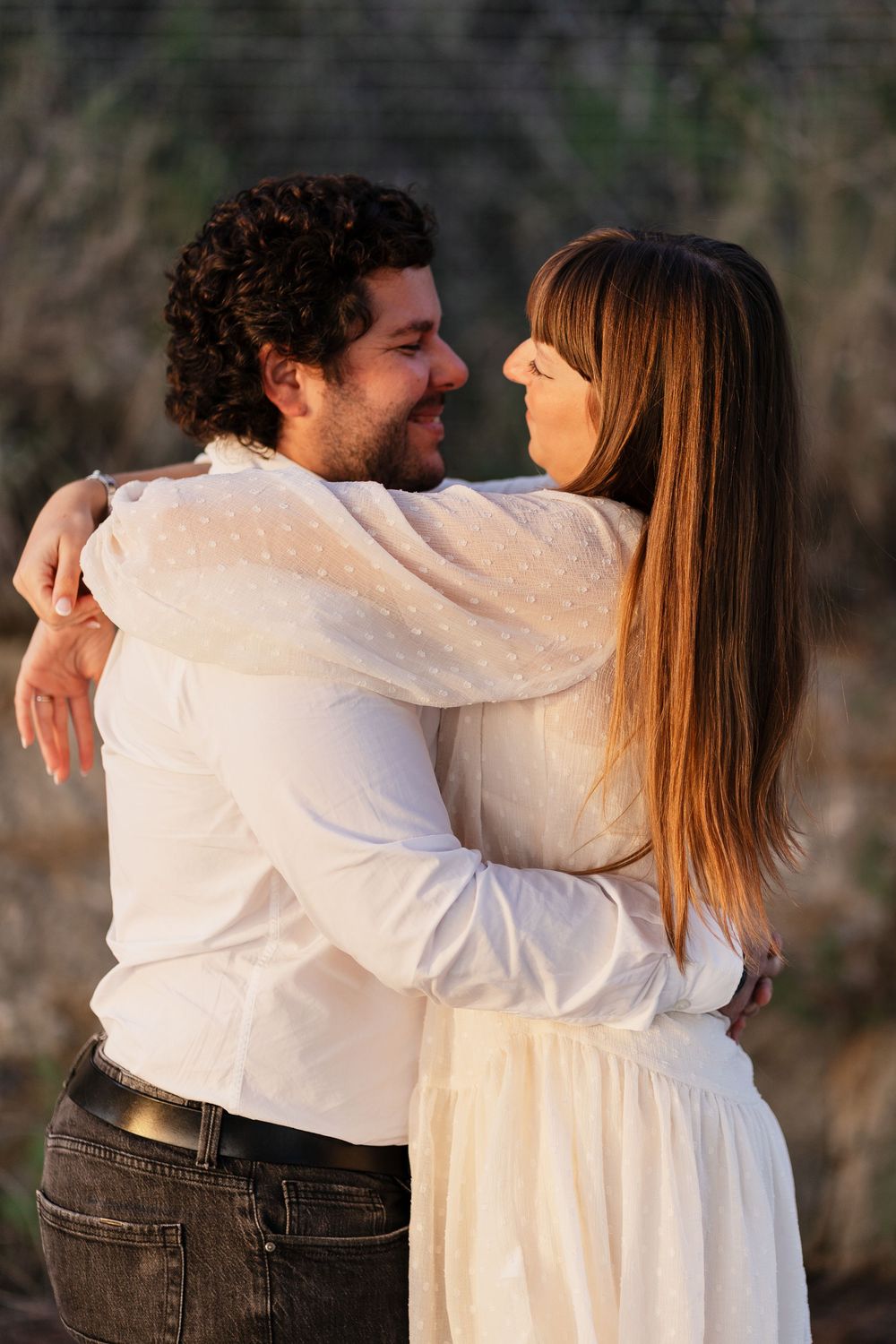 A couple in white and denim embrace and dance together on a scenic outdoor path at dusk.