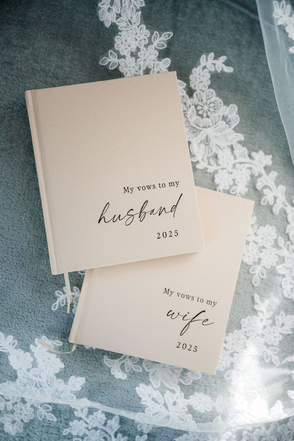 Wedding vow booklets labeled 'husband' and 'wife' with 2025 date on lace background.