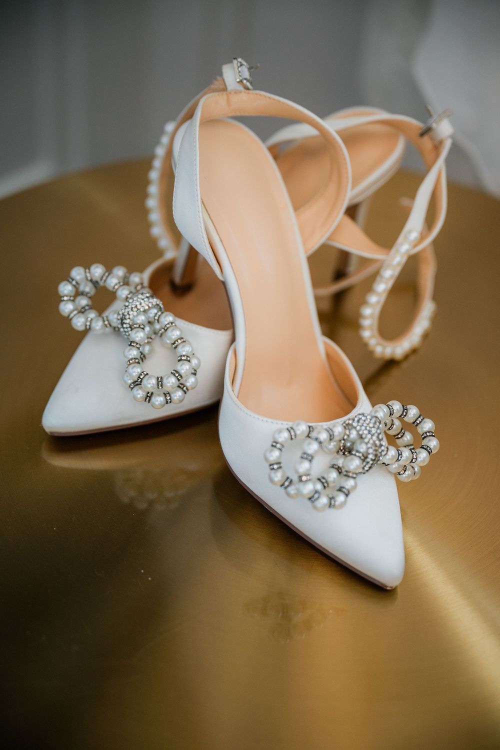 Elegant white bridal shoes with crystal embellishments displayed on a golden surface.