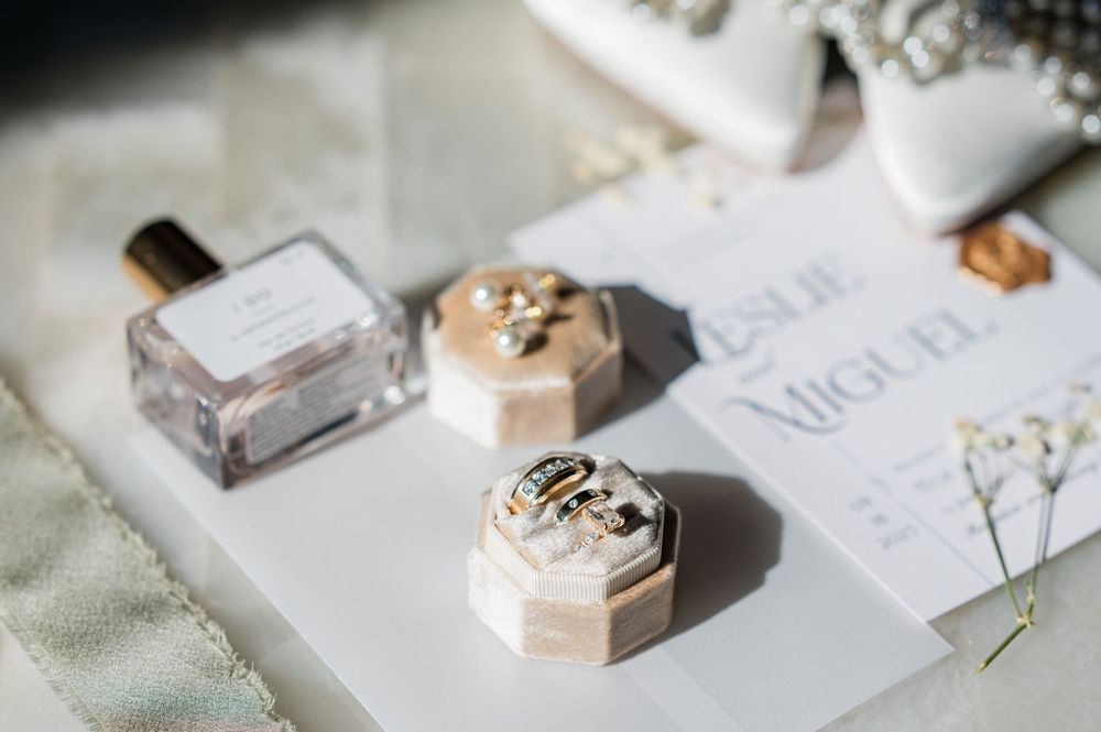 Flat lay of minimalist wedding stationery and accessories in white and metallic tones.