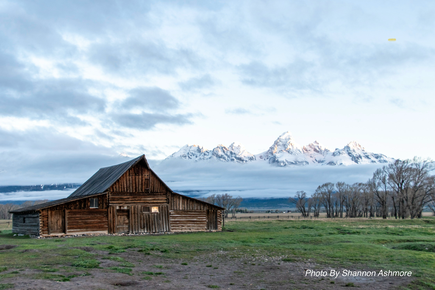 Historic Mormon Row barn with snow-capped Grand Teton mountains in background at sunrise.