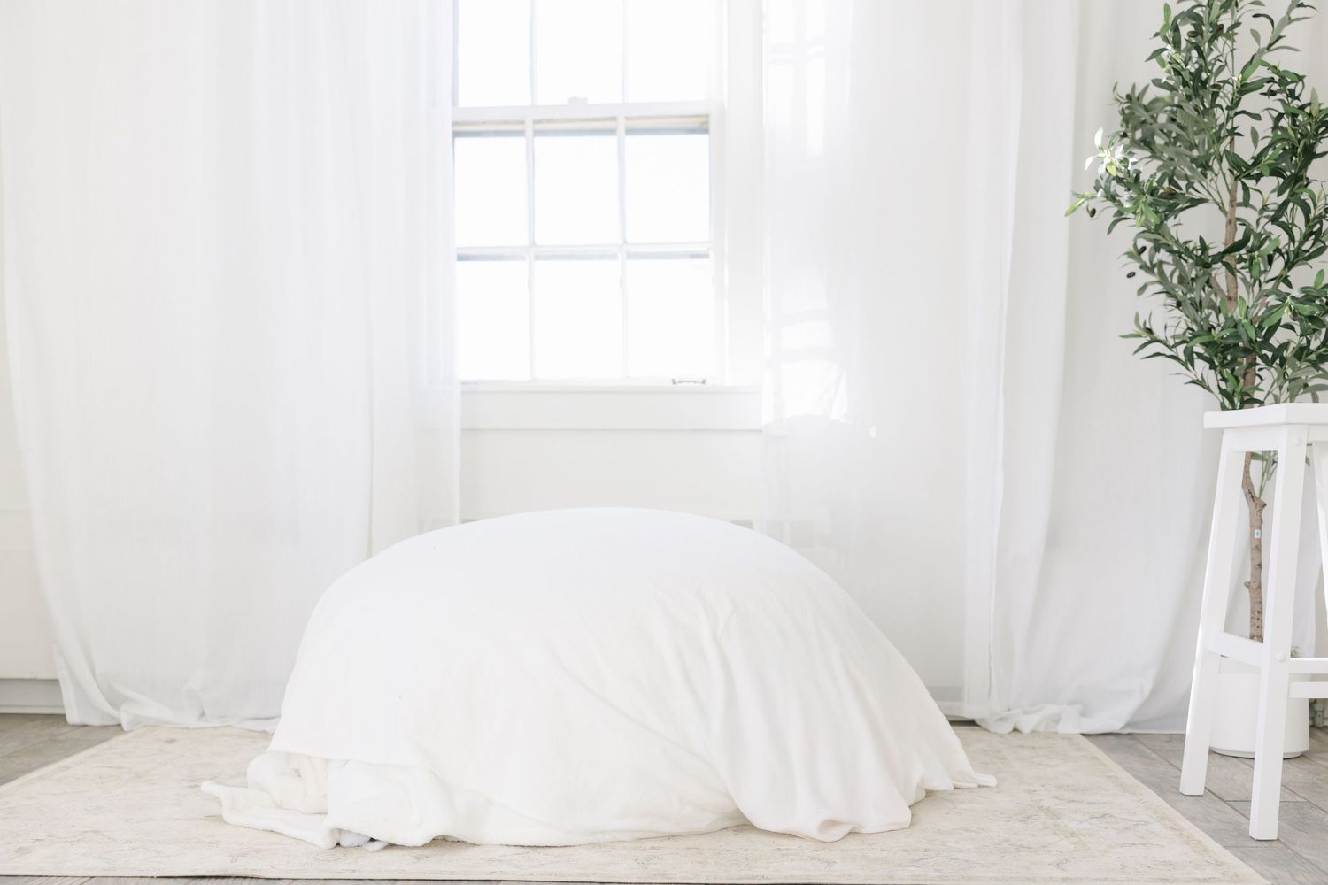 White bedding and linens in a bright, airy bedroom with natural light and green plants by the window.