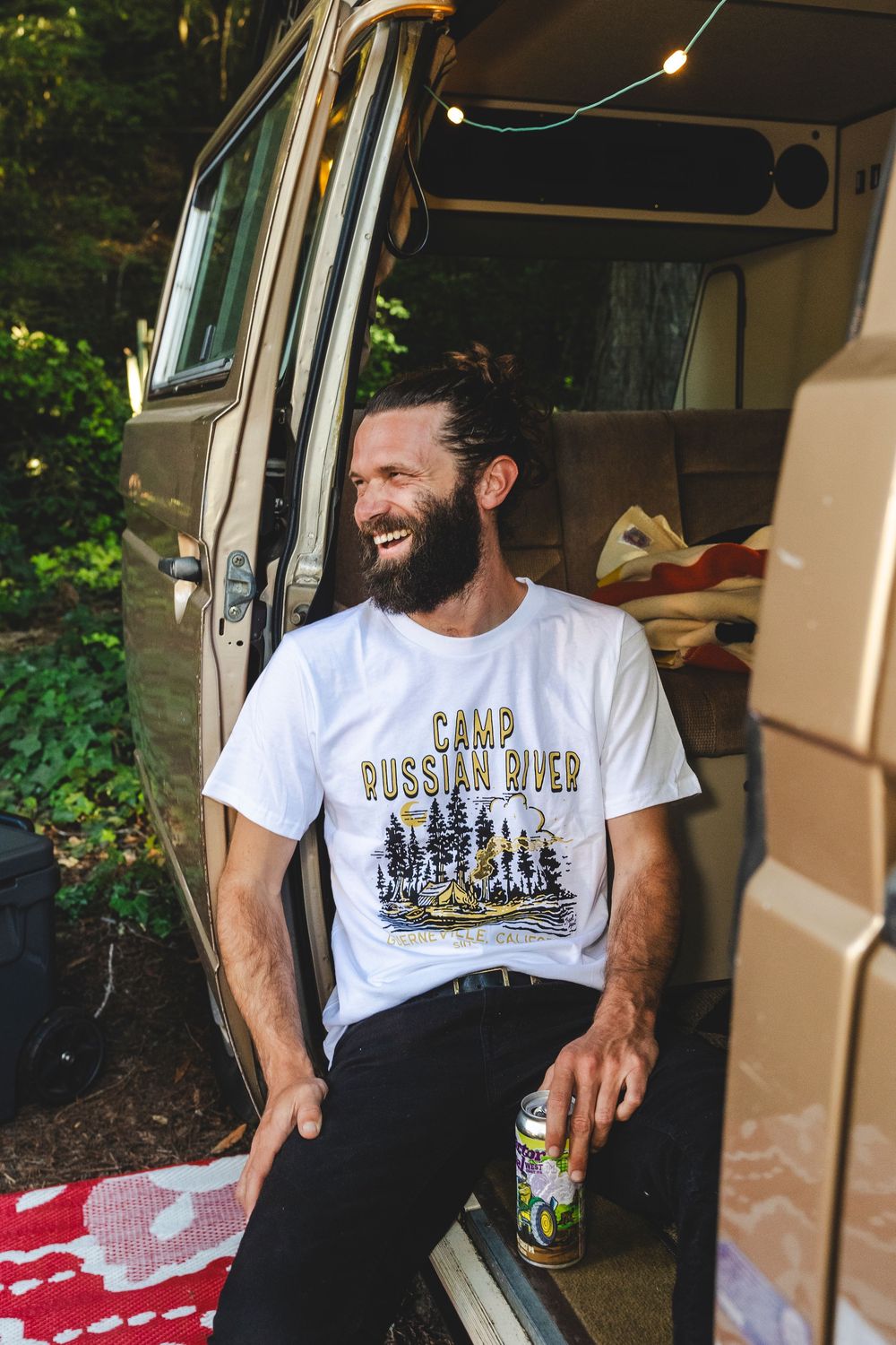Person sitting in a van wearing different t-shirts with outdoor-themed graphics and text.