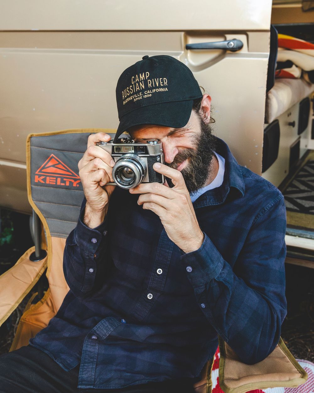 Person in blue jacket taking photos with a vintage camera against a wooden background.