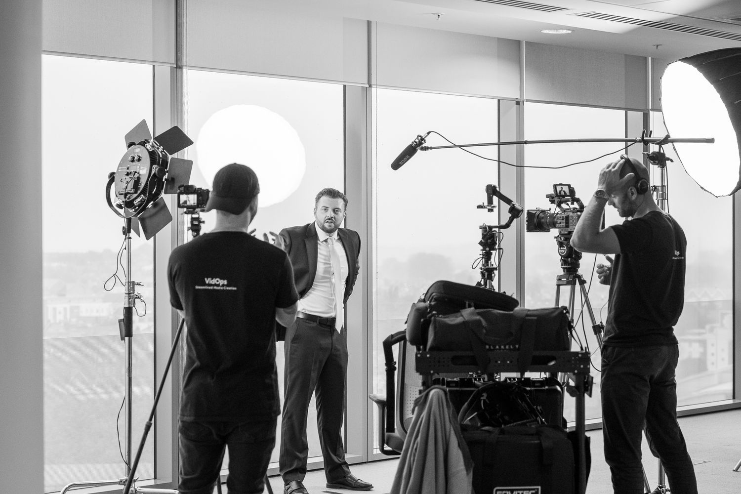 Behind the scenes photo shoot setup with lighting equipment, cameras, and crew members in a bright studio space.
