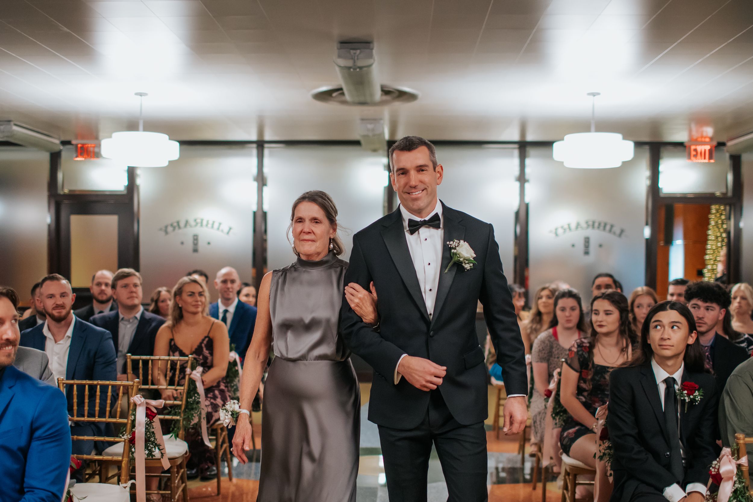 A processional moment at a wedding ceremony with guests seated in rows watching the aisle.