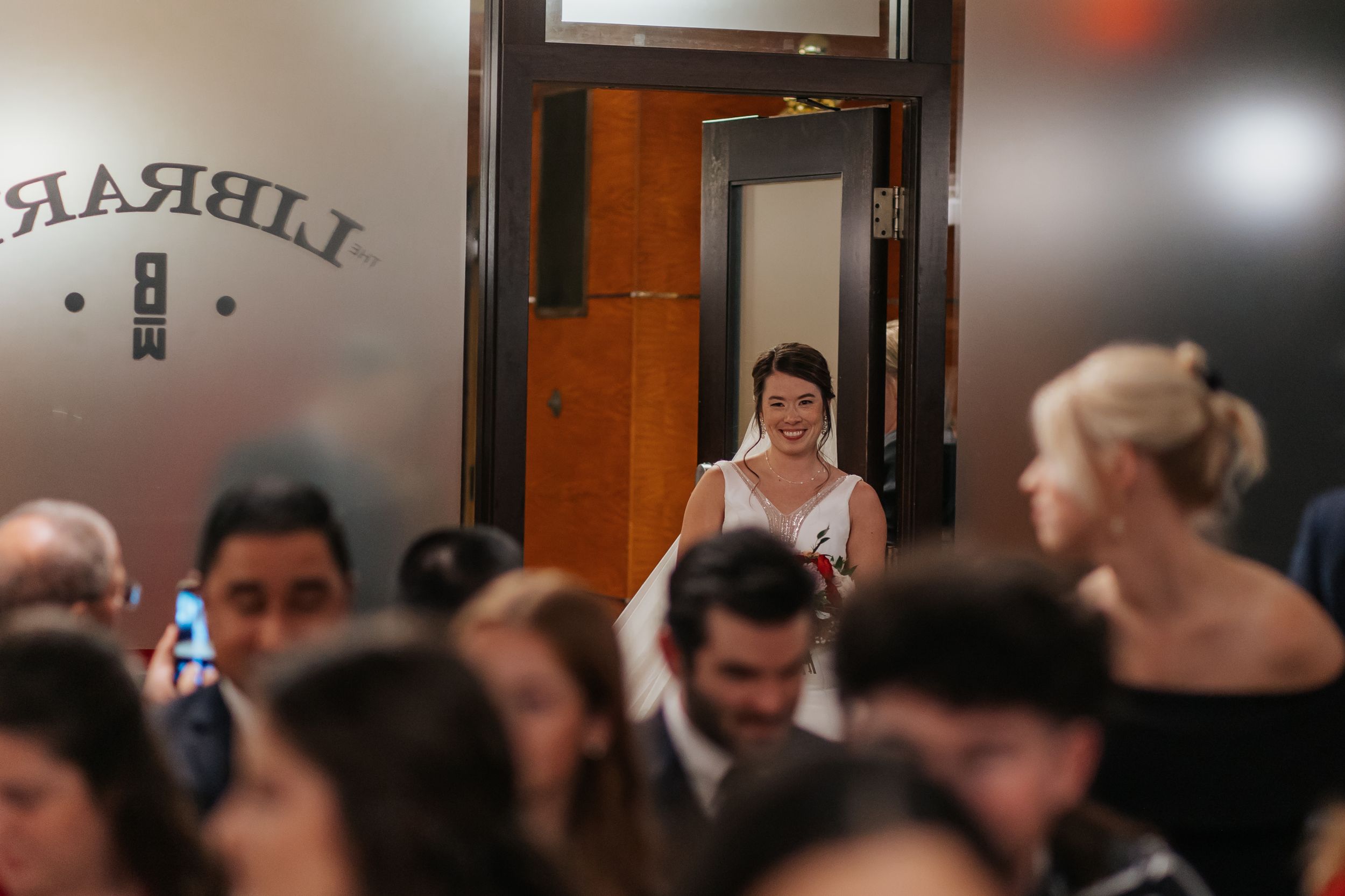 A crowded bar or restaurant interior with patrons seated at tables and standing in a dimly lit space.