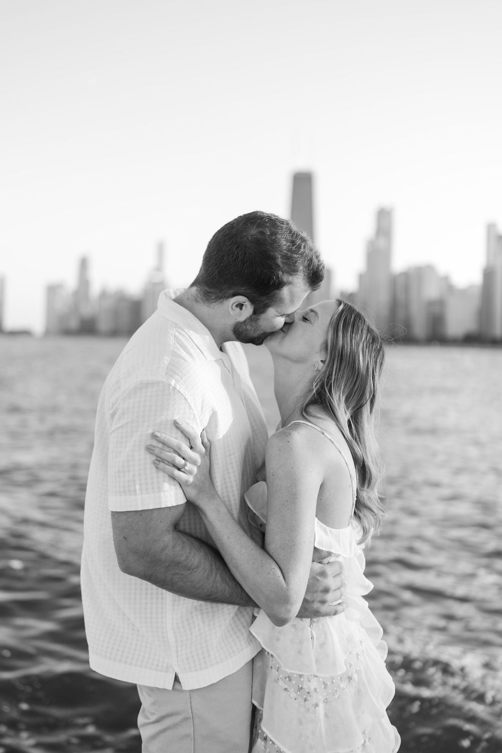 A romantic couple embraces by the water with a city skyline in the background, shown in a series of black and white photos.