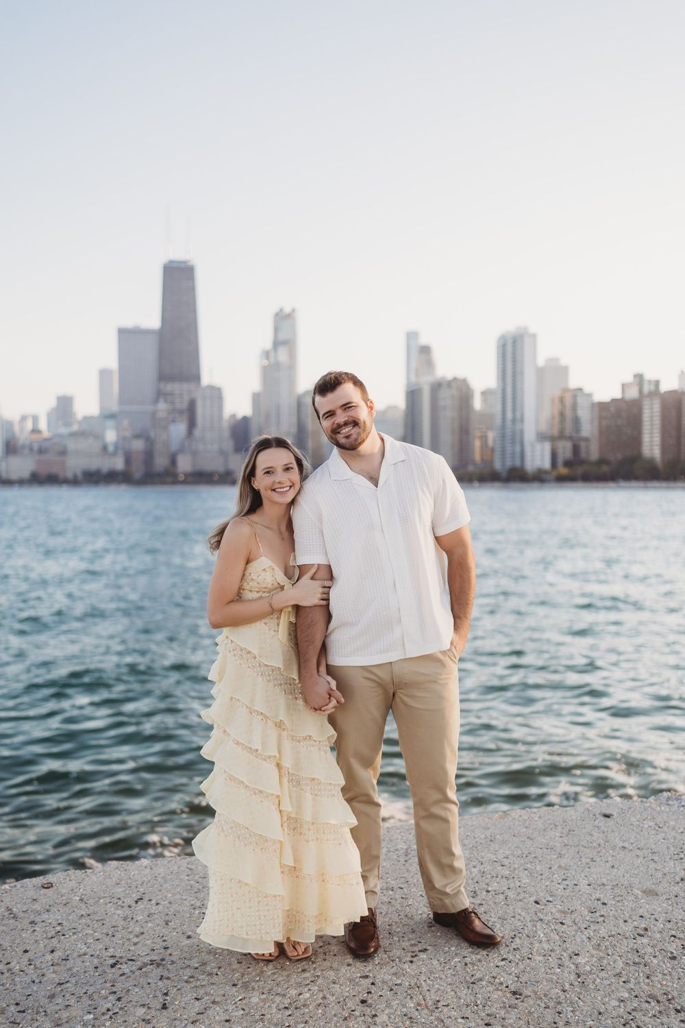 A couple poses romantically against the Chicago skyline backdrop along Lake Michigan during a sunset photoshoot.