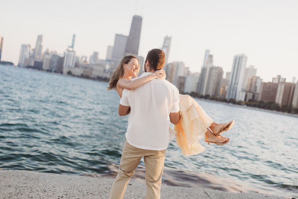 Couple dancing and laughing together on beach with city skyline and water views.