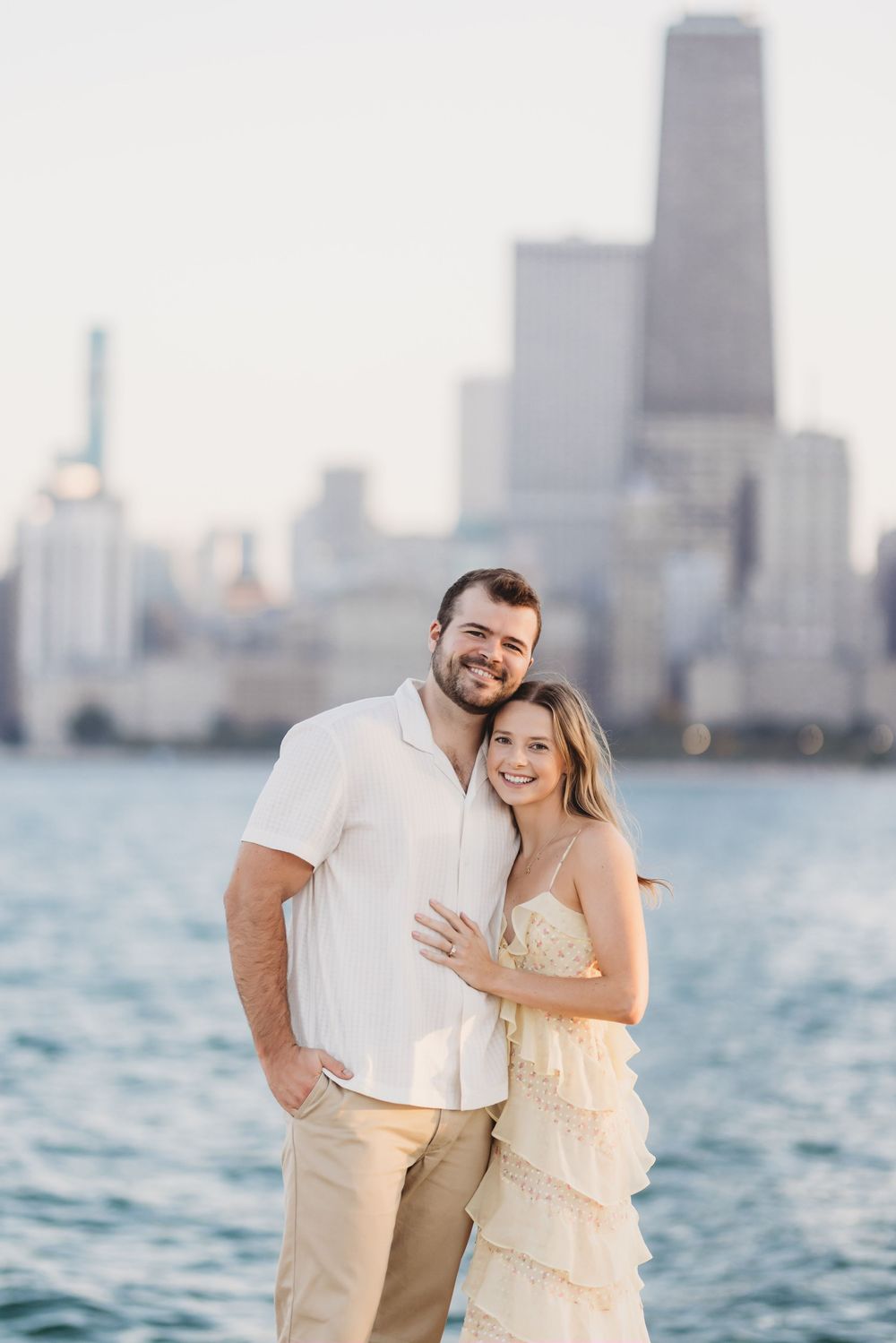 Happy couple embraces on lakefront with Chicago's iconic skyline and blue waters in background.