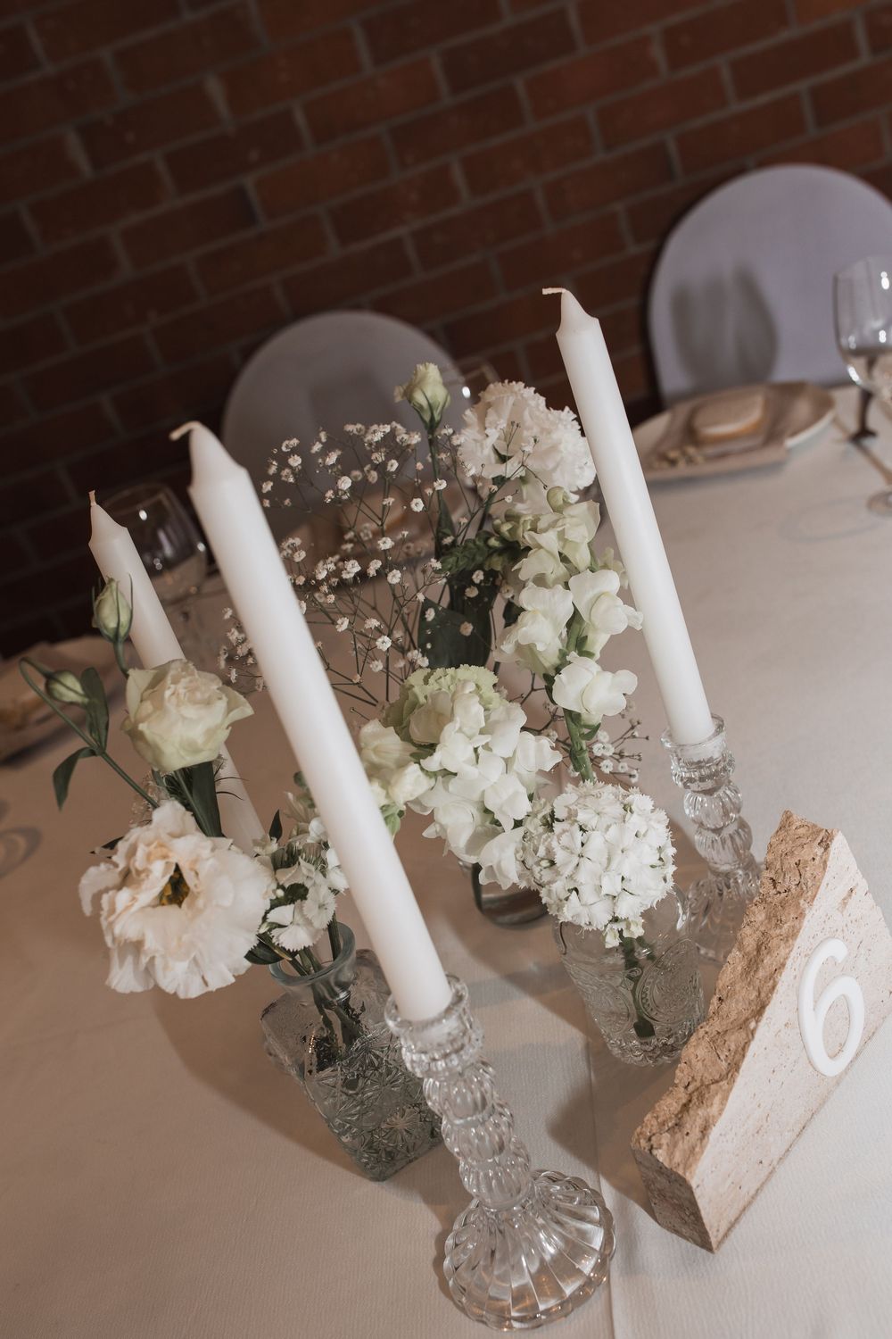 White taper candles and delicate floral arrangements in crystal vases create an elegant table centerpiece display.
