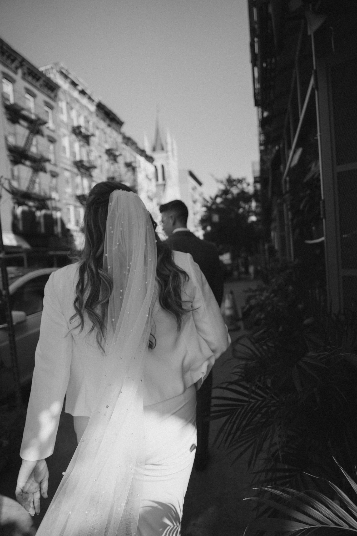 A couple walks down a city street at sunset with buildings casting long shadows.