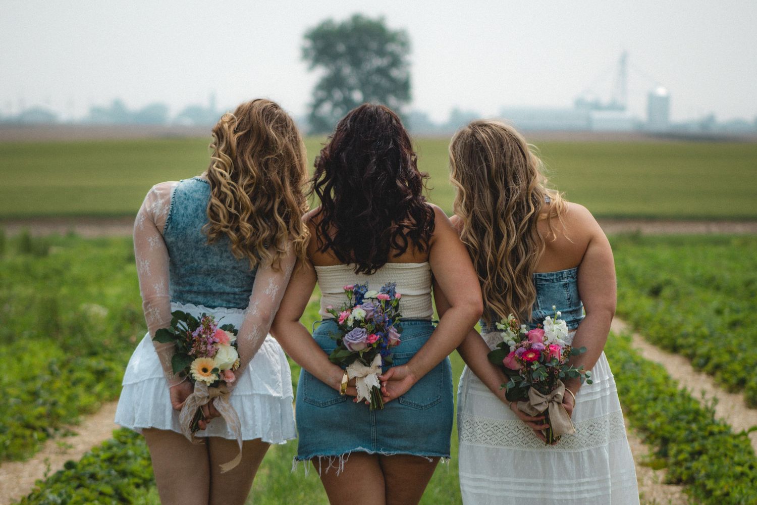three sisters looking in the horizon with flowers behind their backs