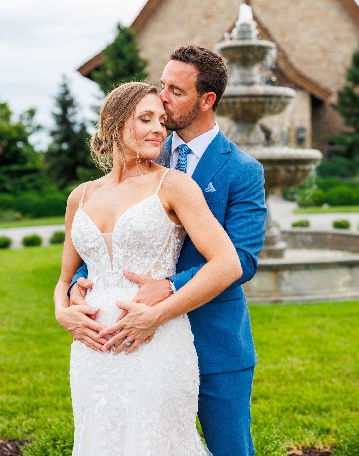 A couple walks hand in hand on a stone path outside a rustic chapel with beautiful landscaping.