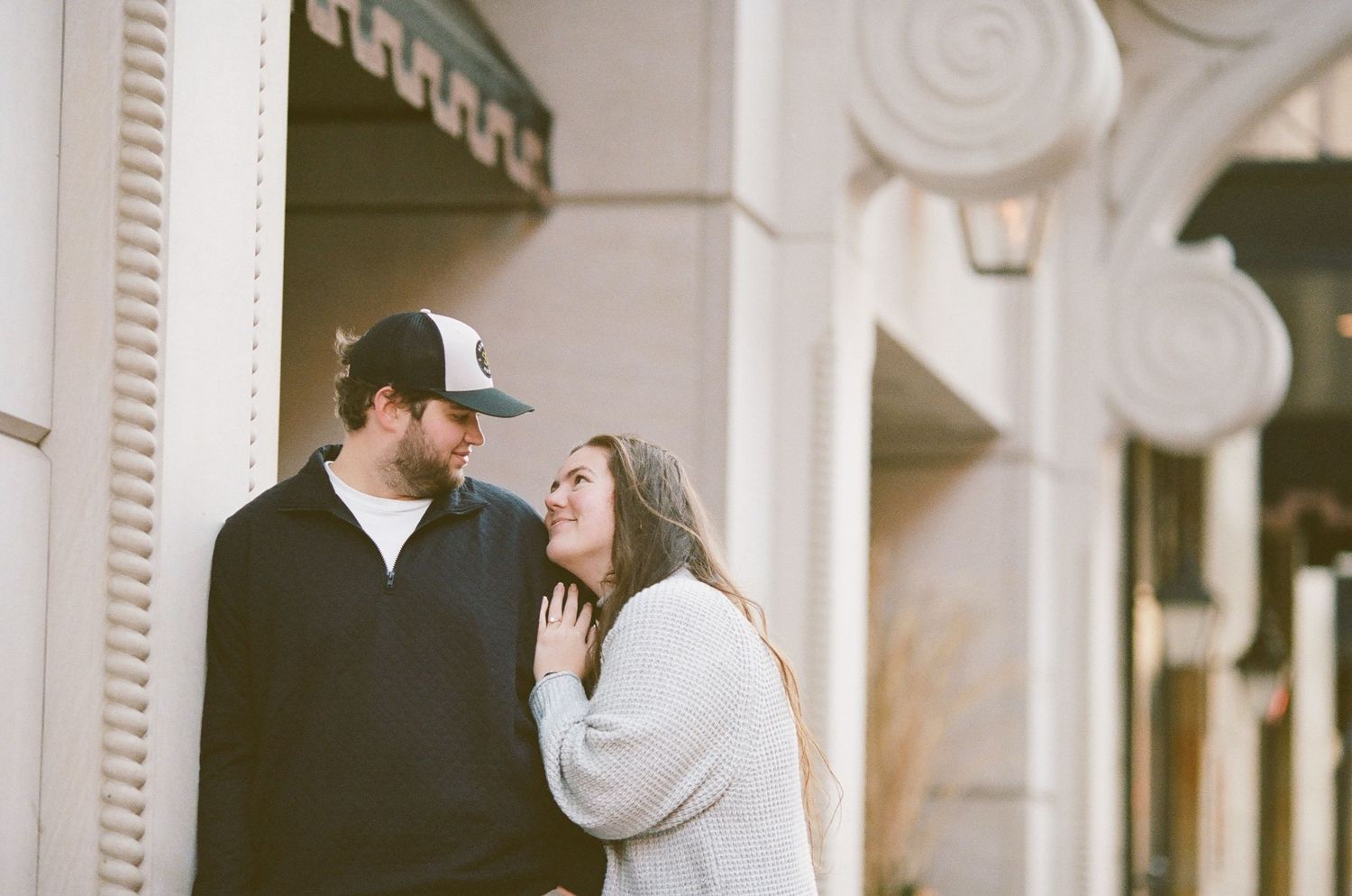 A couple shares a tender moment together outside a building with ornate architectural details.