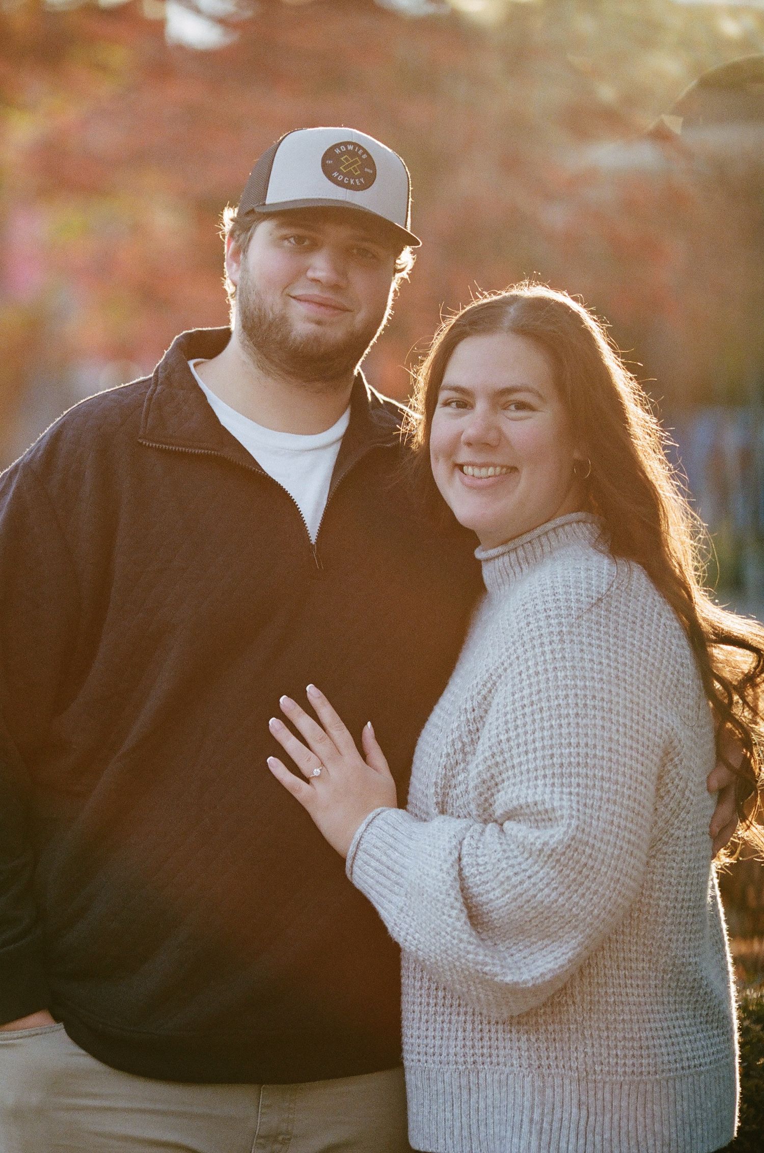 Romantic couple embraces outdoors during golden hour sunset in autumn setting.