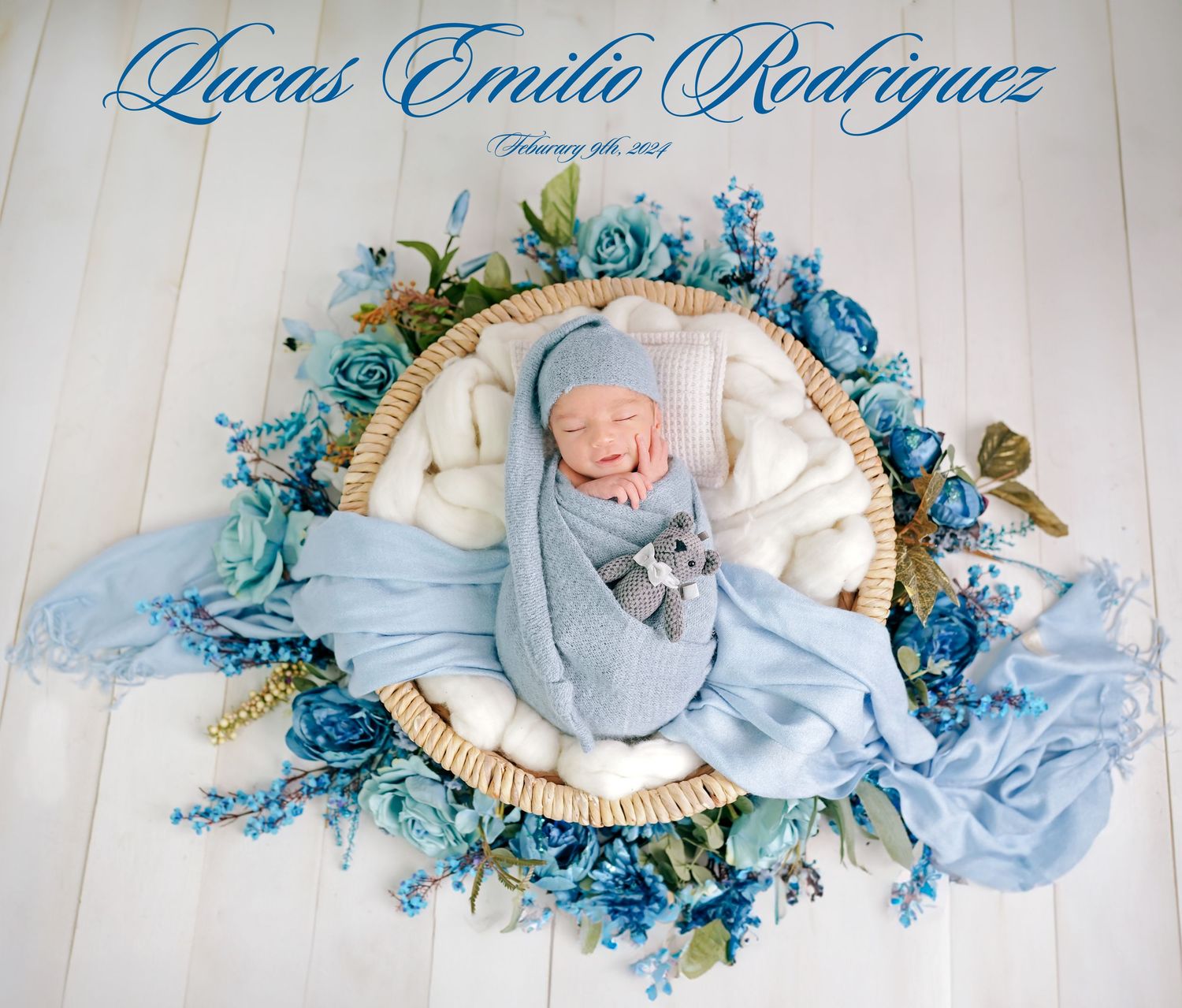 Newborn baby in light blue outfit lying on white blanket with blue floral wreath and decorative elements.