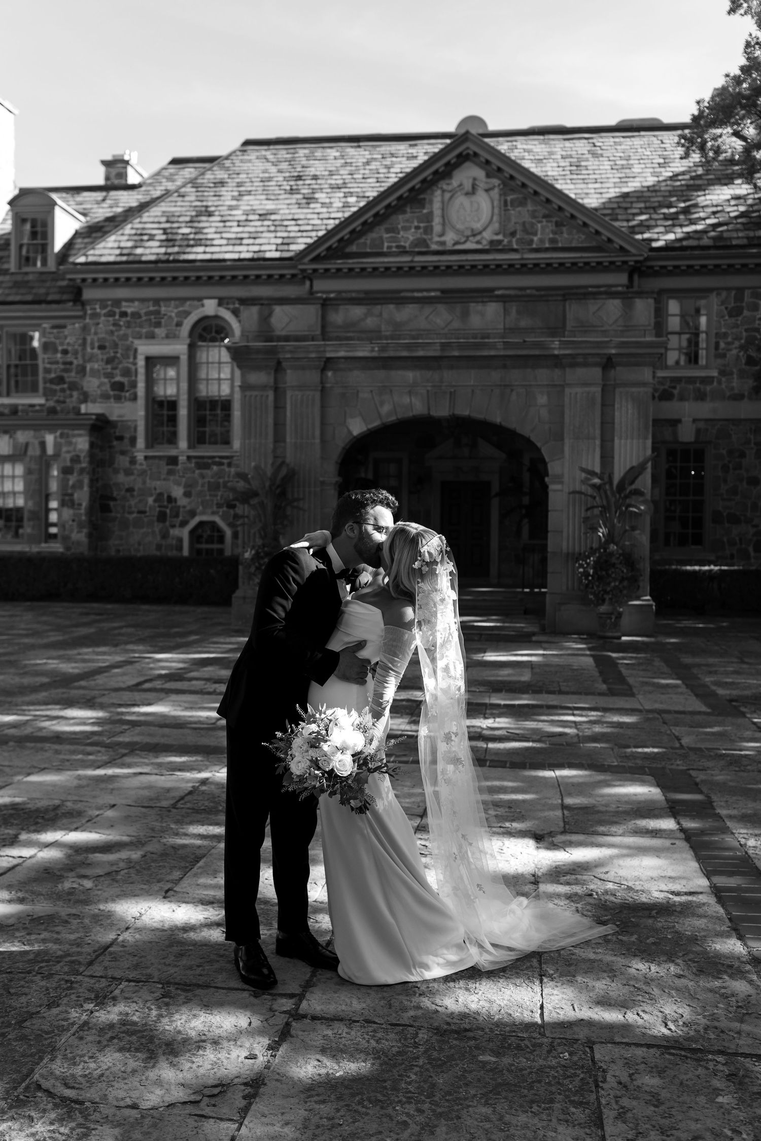 A black and white wedding photo showing a couple holding hands, with the bride in a lace veil and the groom in a tuxedo.