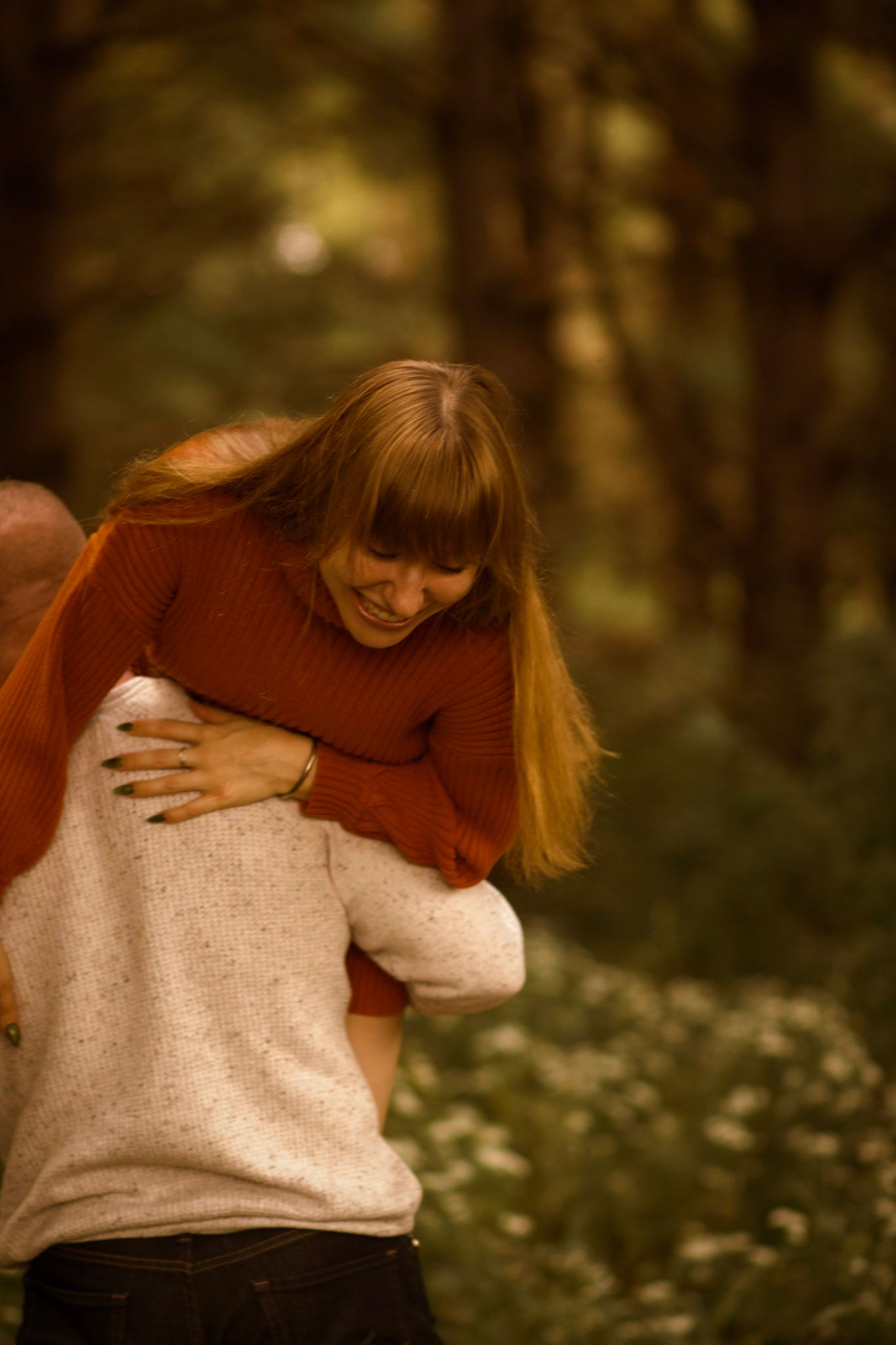 Two people in cozy sweaters share a tender embrace outdoors among autumn foliage in warm lighting.