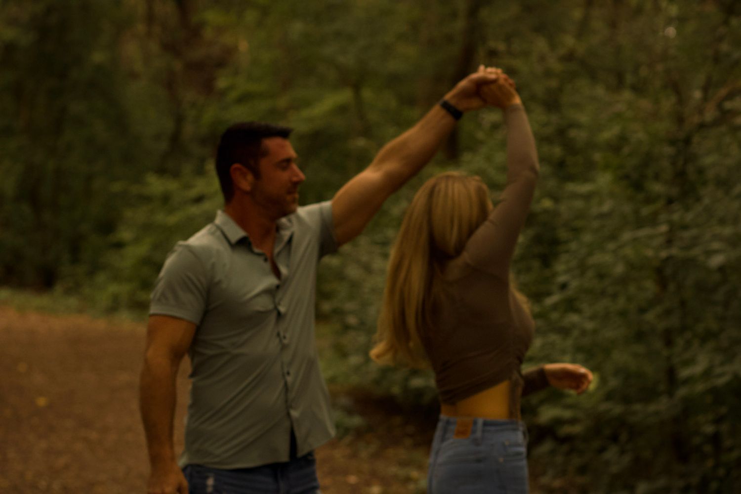 A couple dancing together on a dirt path in a misty forest setting during golden hour.