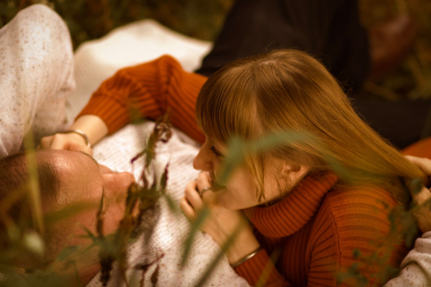 A person wearing an orange sweater holds a small brown and white guinea pig in their hands.