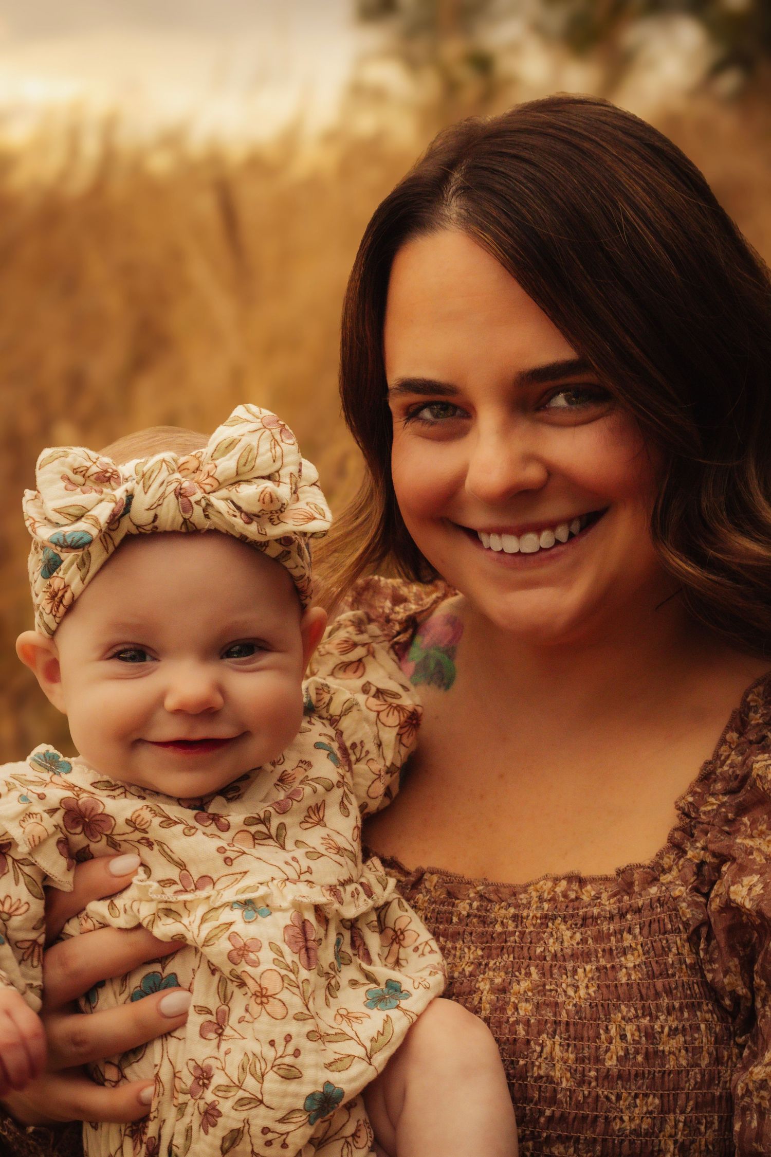 A warm portrait of a parent and baby in matching floral outfits smiling together against a golden outdoor background.