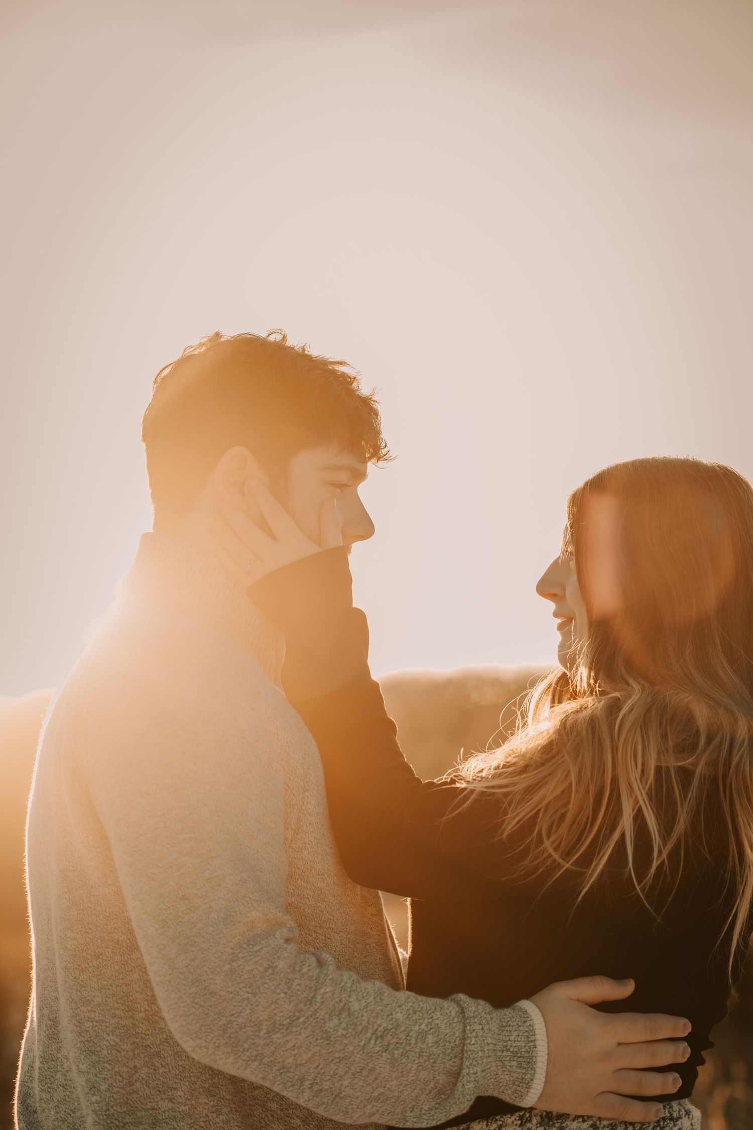 Romantic silhouette of couple embracing during golden hour sunset with warm backlight creating atmospheric glow.