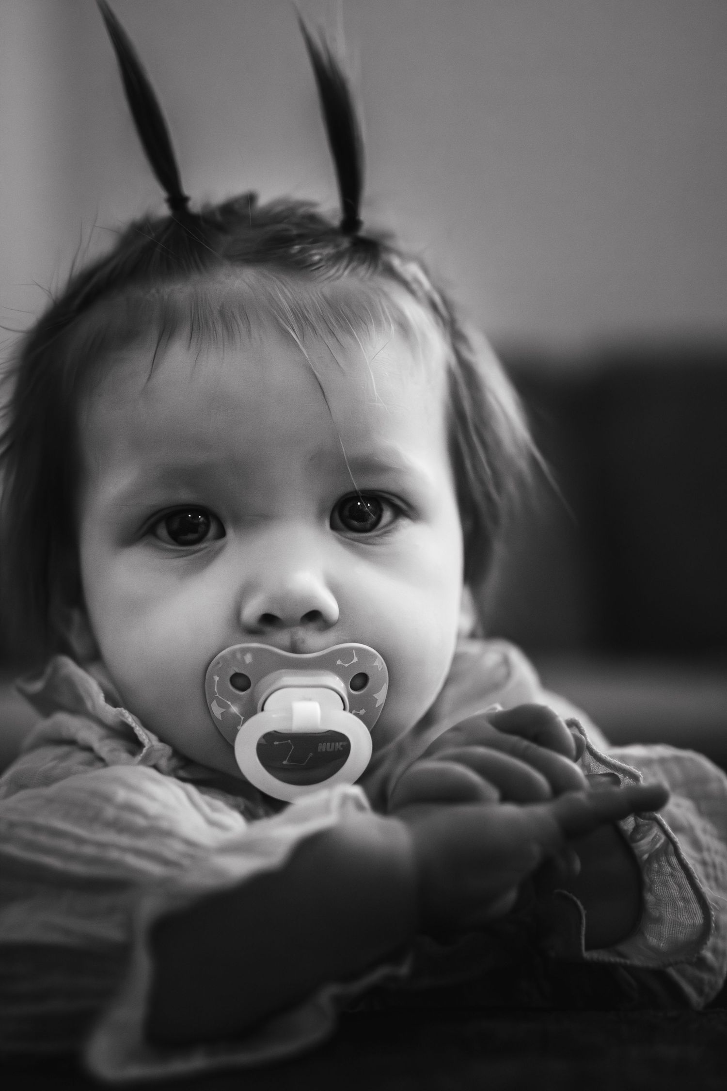 A black and white portrait of a small child with pigtails and a pacifier looking directly at the camera.