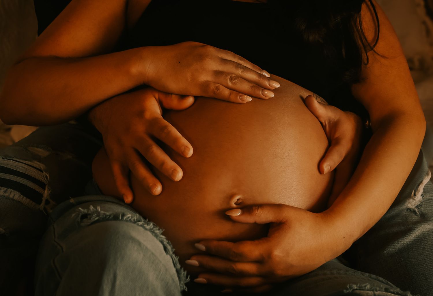 Close-up of a pregnant woman's belly being gently touched by hands in a tender maternity photo series.