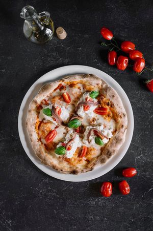 Pizza rustica italiana con pomodori freschi e foglie di basilico su uno sfondo di pietra scura.