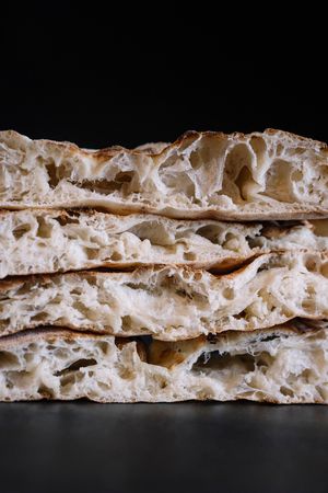 Vista ravvicinata della sezione trasversale degli strati della pinsa che mostra una delicata trama a nido d'ape su sfondo scuro.