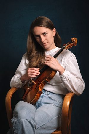 Una musicista con una camicetta di pizzo bianco e jeans in posa con il suo strumento.
