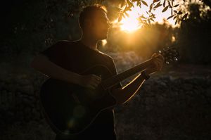 Sagoma di chitarrista durante il tramonto in Puglia, in mezzo agli ulivi