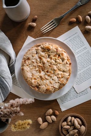 Una torta rustica è appoggiata su un tavolo di legno con mandorle sparse e pagine di ricette.