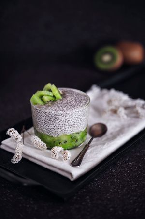 Un dessert a strati a base di budino di chia con guarnizione di kiwi e tovagliolo di pizzo bianco su sfondo scuro.