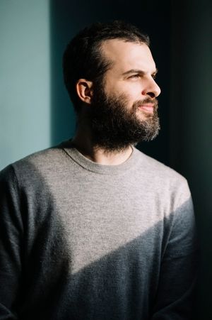 Profilo laterale di una persona che indossa un maglione grigio su uno sfondo chiaro con ombre drammatiche.