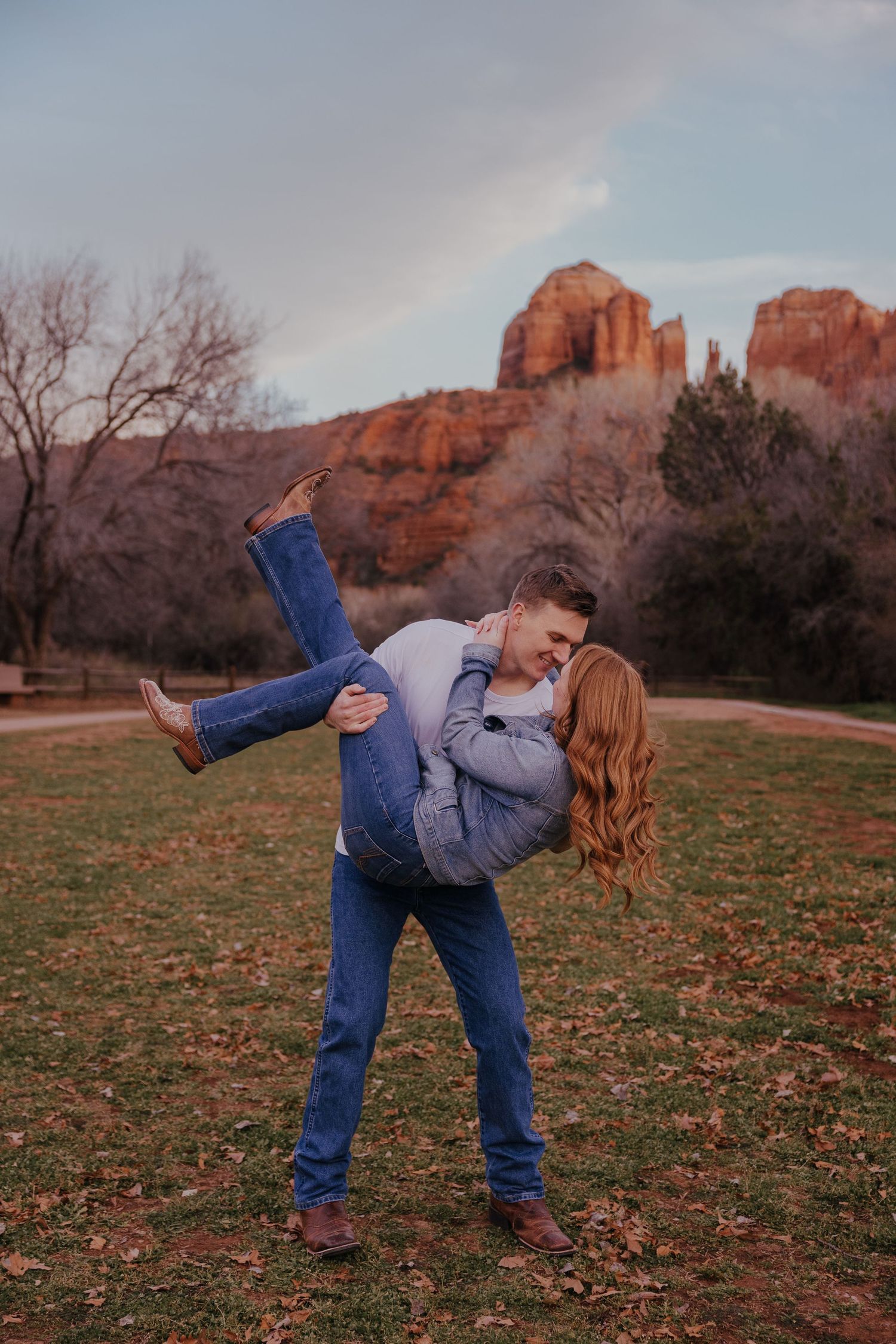 Playful couple dancing together in a field with red rock formations in the background at sunset.