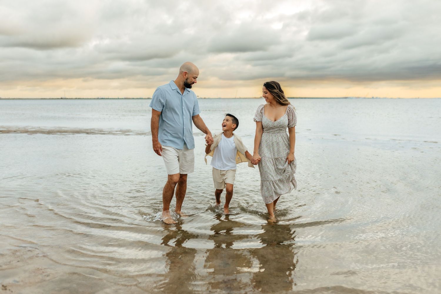 Family holding hands while walking along the beach during a lifestyle photography session.