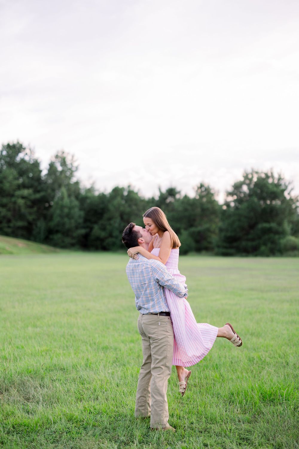 Two people share a romantic spin and embrace in an open green field.
