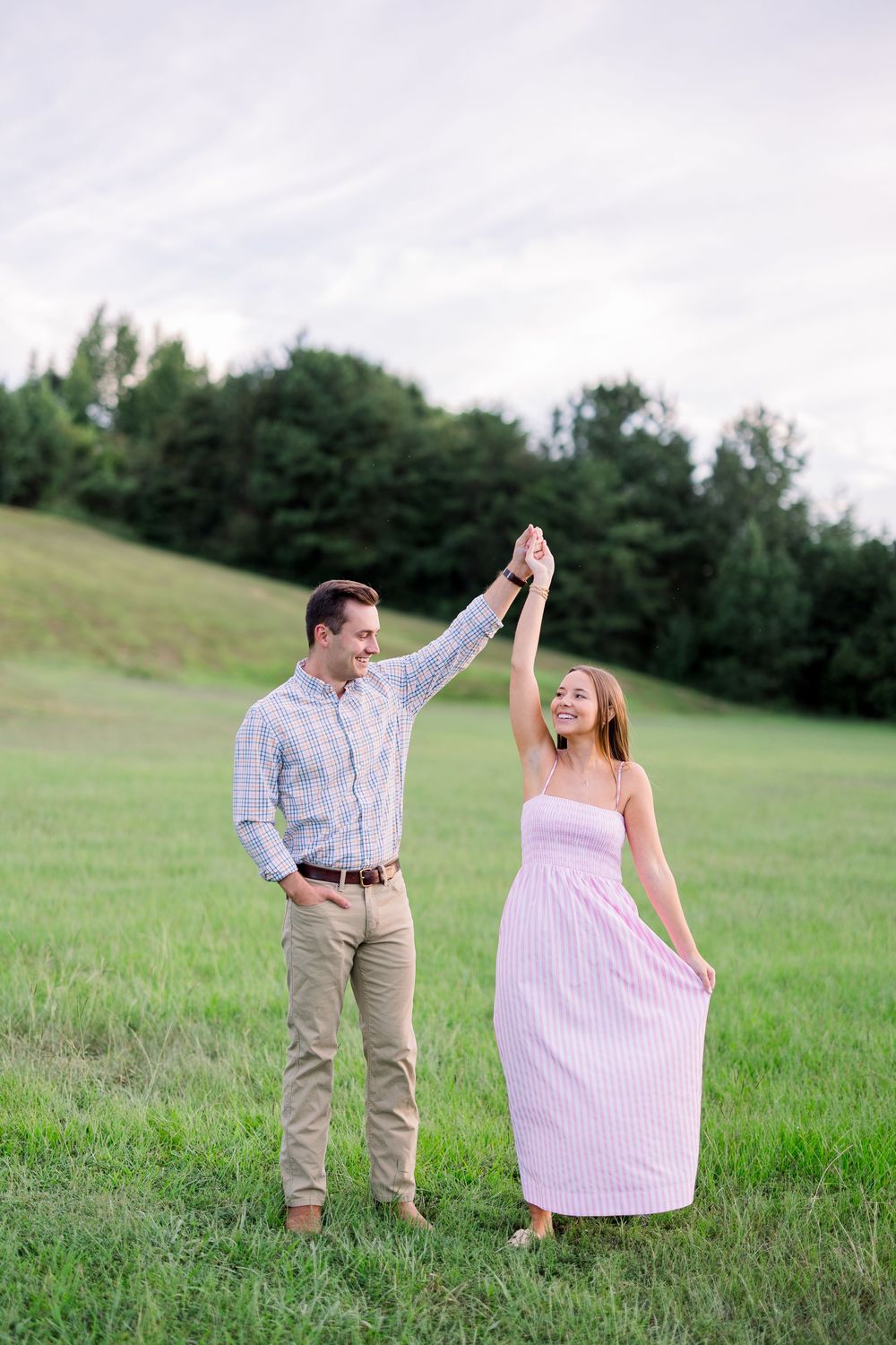 A couple in casual attire dances together on a sunny afternoon in a grassy field.