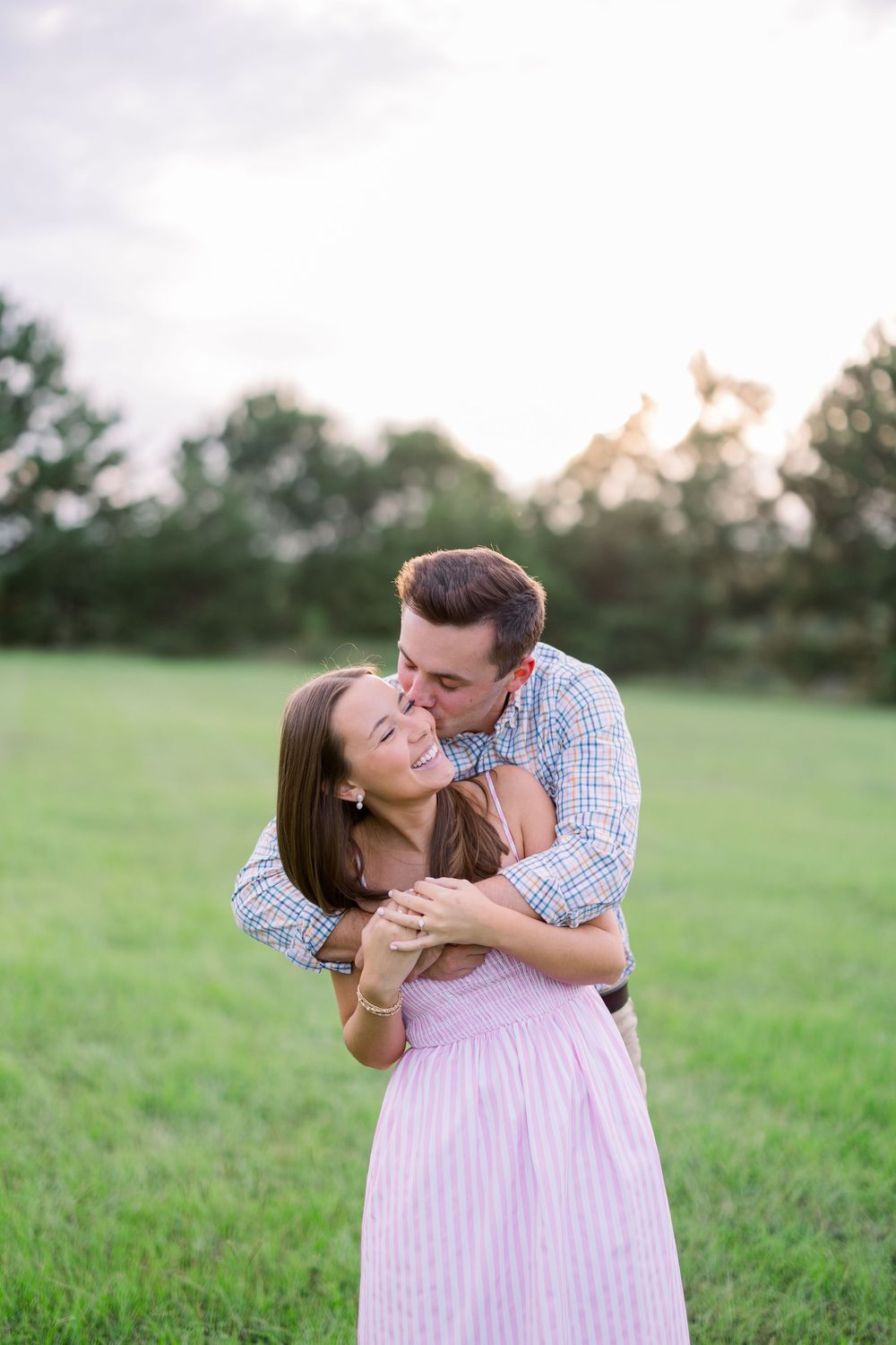 A tender embrace shared between two people in a summer field at golden hour.